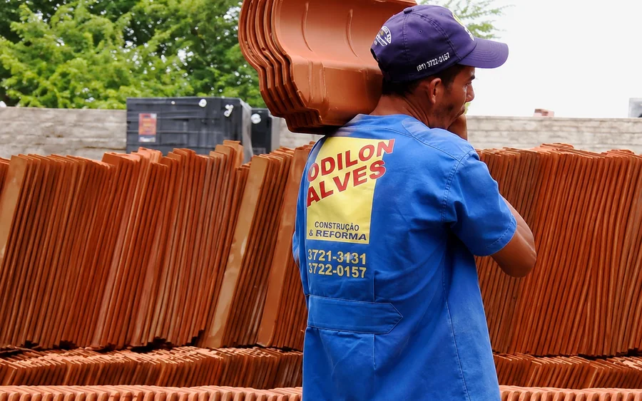 Colaborador da Odilon Alves carregando telhas cerâmicas no pátio da loja